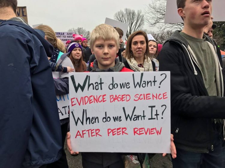boy holding a protest sign demanding peer review