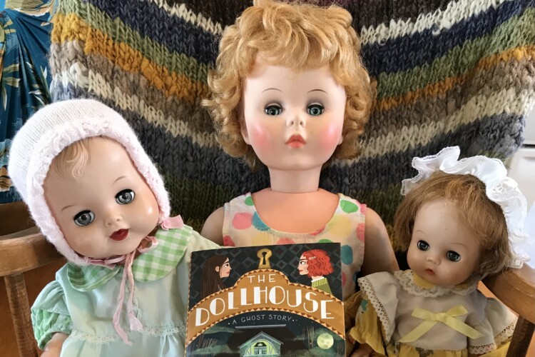 Dolls posed with a copy of The Dollhouse by Charis Cotter